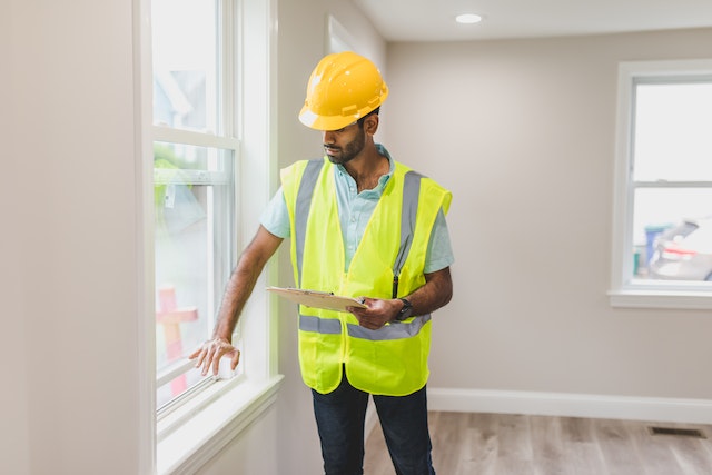 property inspector in reflective vest and hard hat checking home’s windows